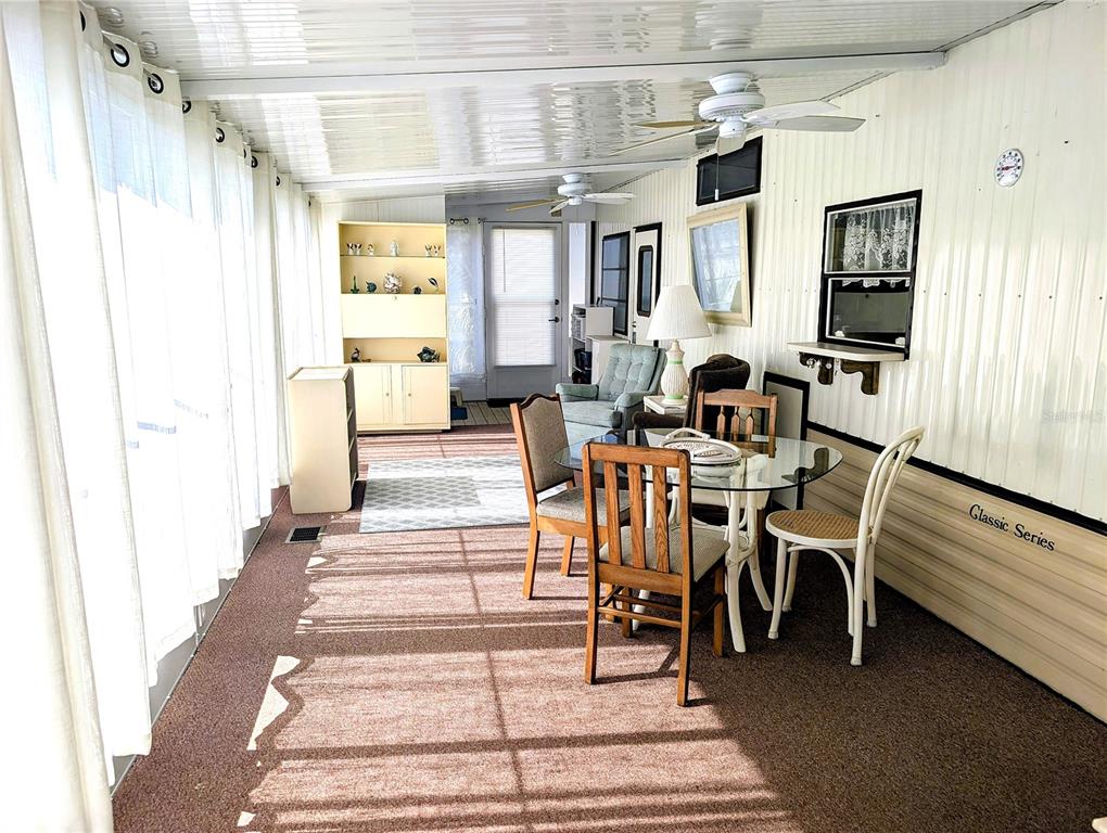 A sunroom features a glass-top dining table, carpeted flooring, and a ceiling fan — 3300 26TH AVENUE E UNIT 31, BRADENTON, FL