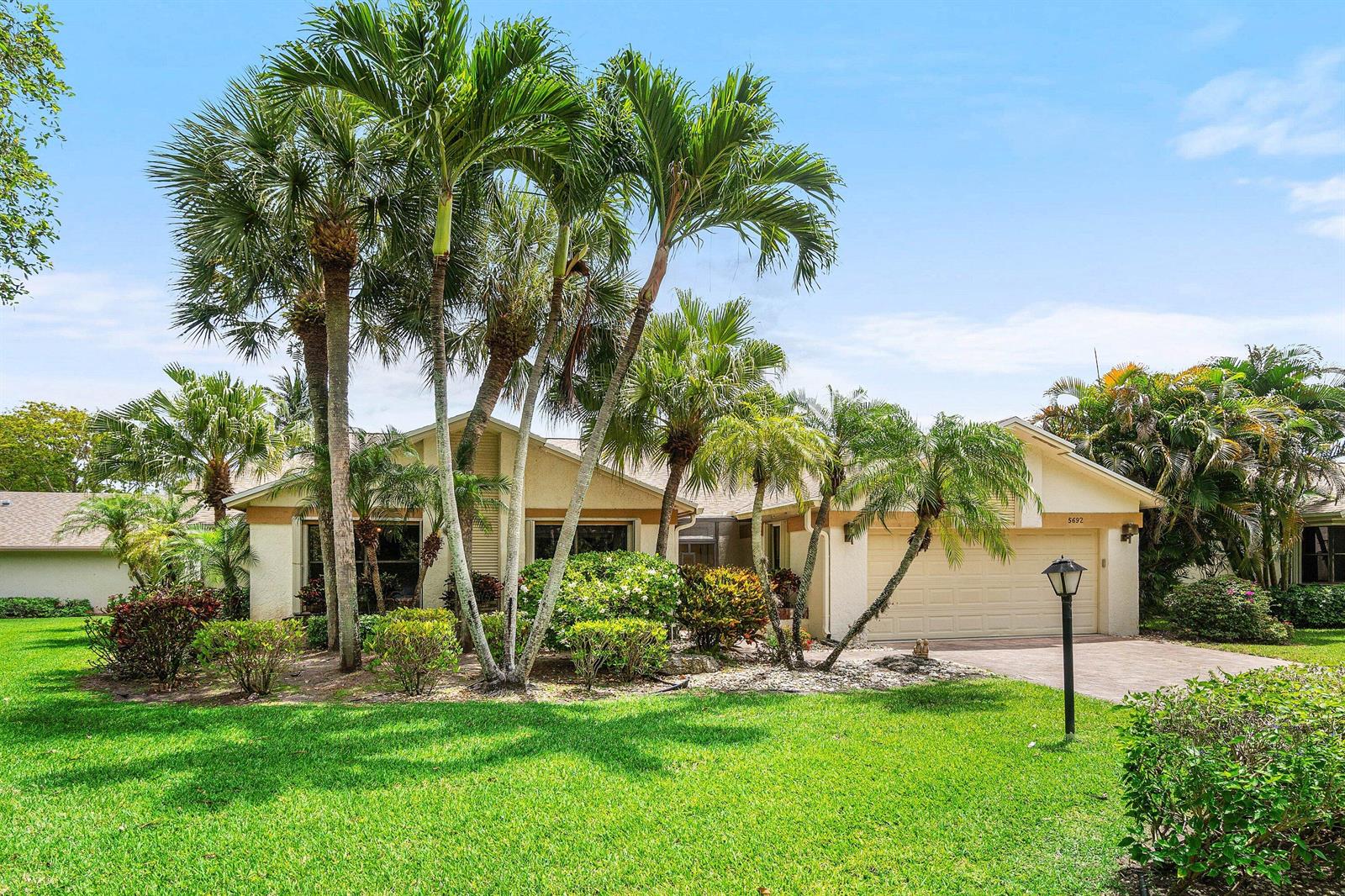 A single-story house with a beige exterior, a two-car garage, and several tall palm trees — 5692 Willow Creek Lane, Delray Beach FL 33484, DELRAY BEACH, FL