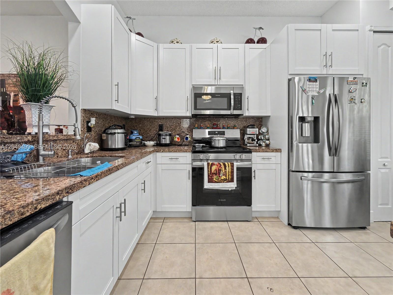 A kitchen features white cabinets, granite countertops, stainless steel appliances, and beige tile flooring — 522 NE 20th Ave, Homestead FL 33033, HOMESTEAD, FL