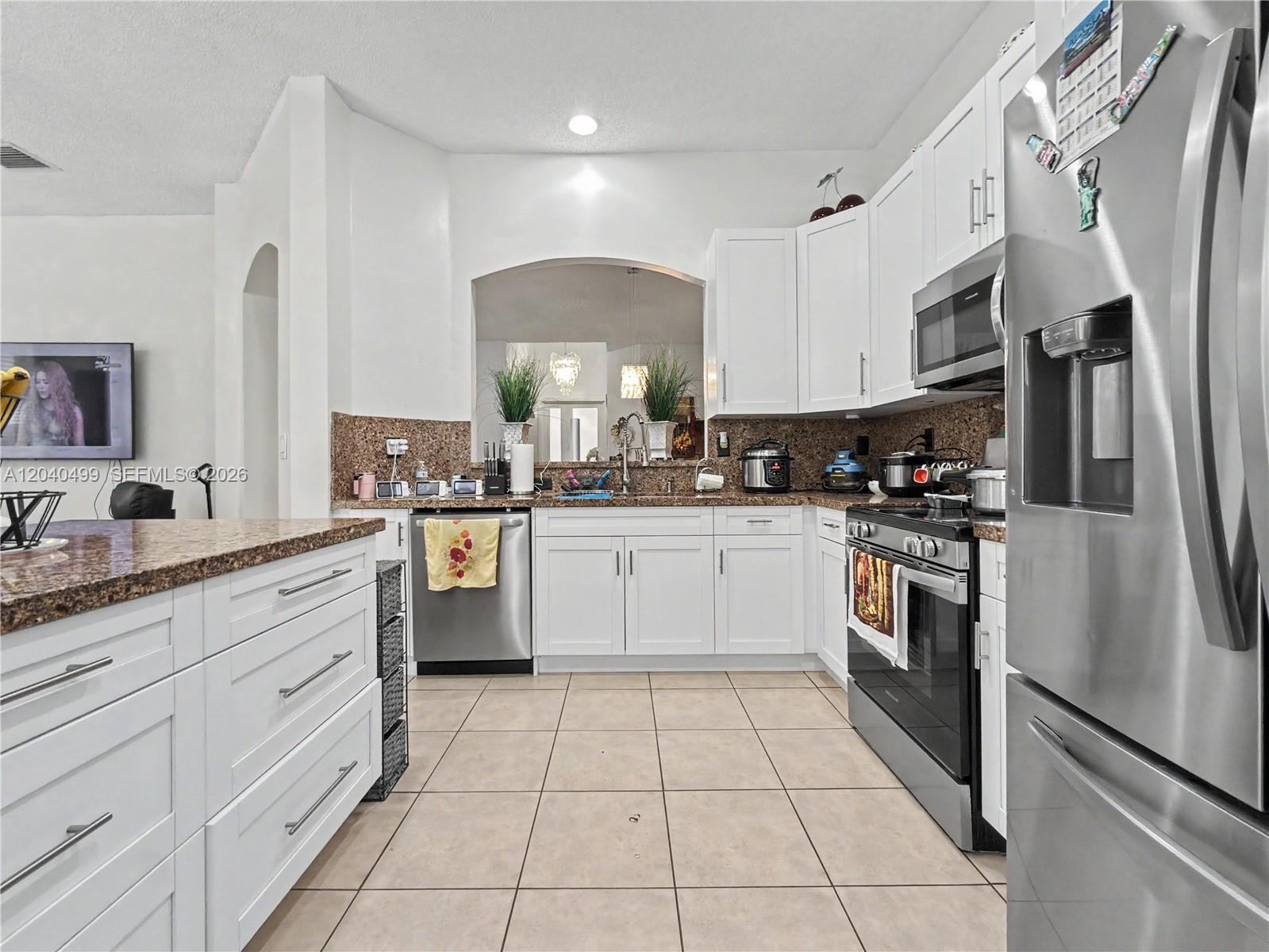 A kitchen features white cabinetry, granite countertops, stainless steel appliances, and beige tile flooring — 522 NE 20th Ave, Homestead FL 33033, HOMESTEAD, FL