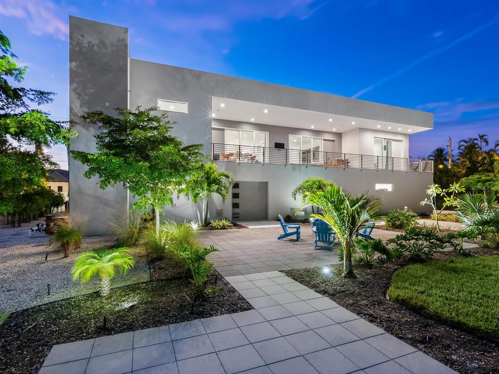 A modern two-story house with a paved patio, balcony, and landscaped yard at dusk — 3939 HIGEL AVENUE, SARASOTA, FL