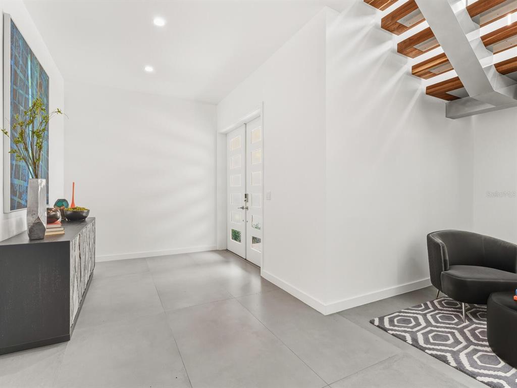 A modern entryway features white walls, large gray floor tiles, a staircase, and double doors — 3939 HIGEL AVENUE, SARASOTA, FL