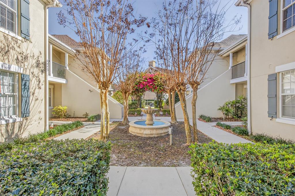 A stone fountain sits in a courtyard between two beige apartment buildings with landscaping — 760 SIENA PALM DRIVE UNIT 204, CELEBRATION, FL