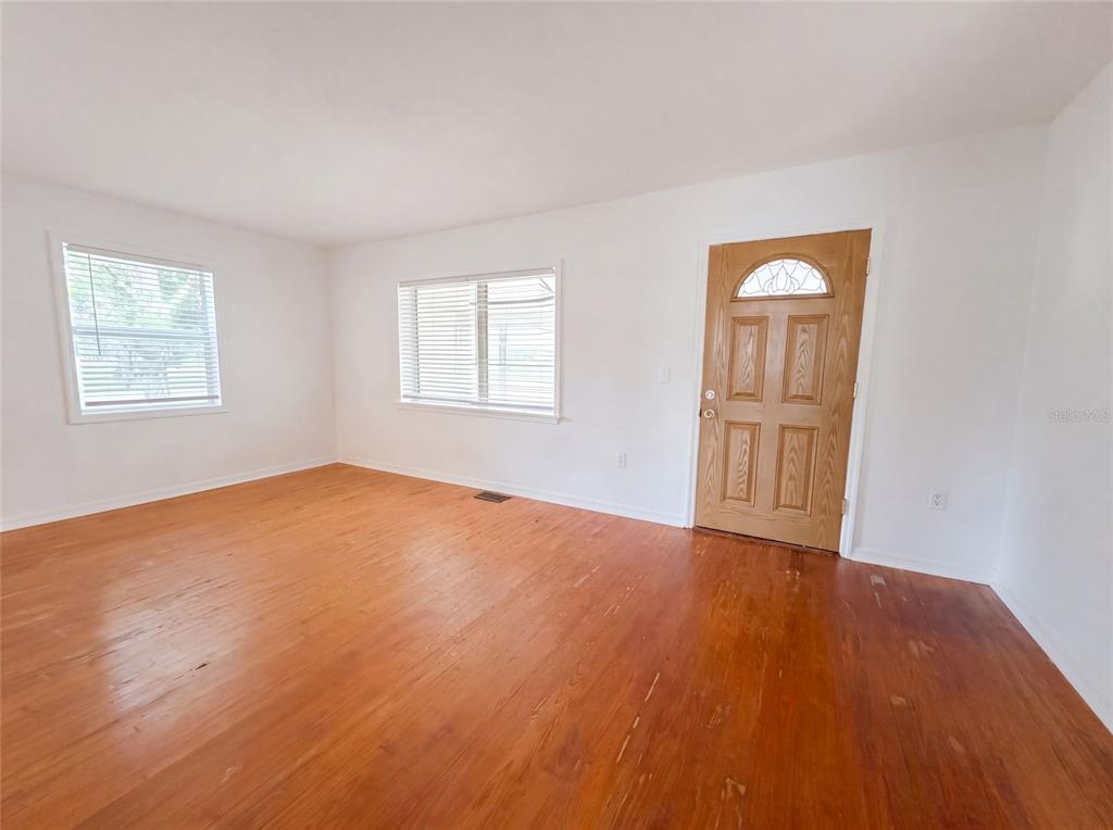 An empty room with white walls, hardwood floors, two windows, and a wooden front door — 2231 9TH AVENUE W, BRADENTON, FL