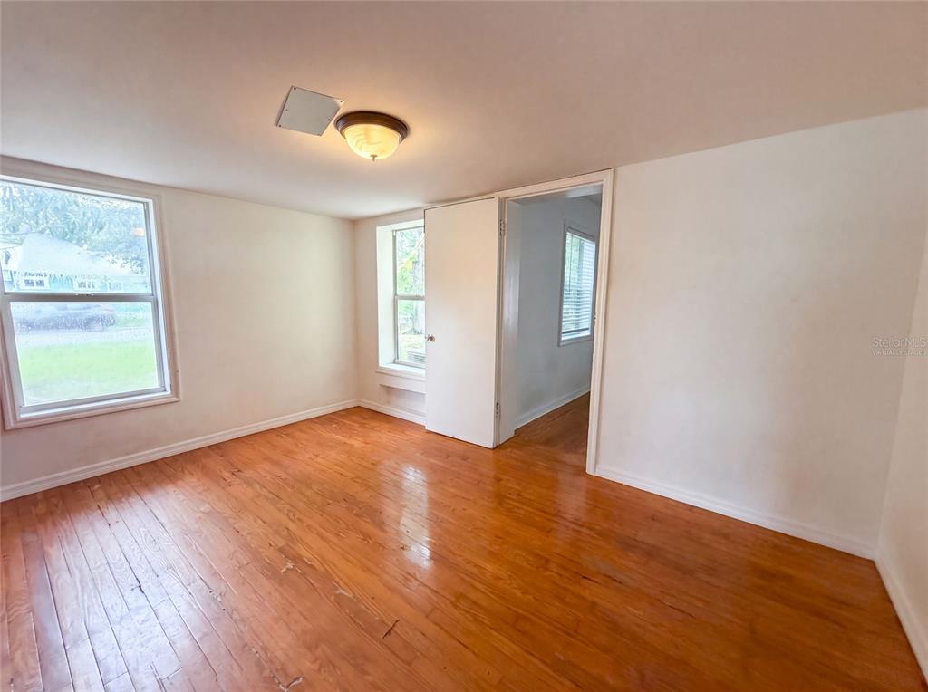 An empty room features hardwood floors, white walls, two windows, and a doorway to another room — 2231 9TH AVENUE W, BRADENTON, FL