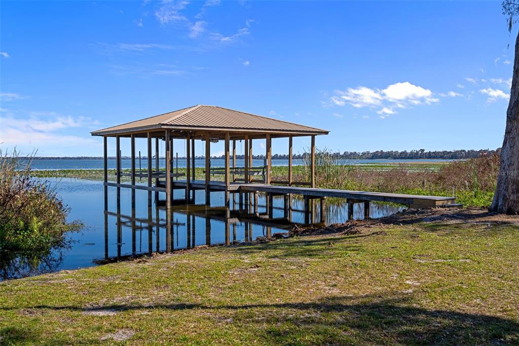 A wooden boat dock with a metal roof extends into a lake from a grassy shore — 4300 TIMBERLANE ROAD, LAKE WALES, FL