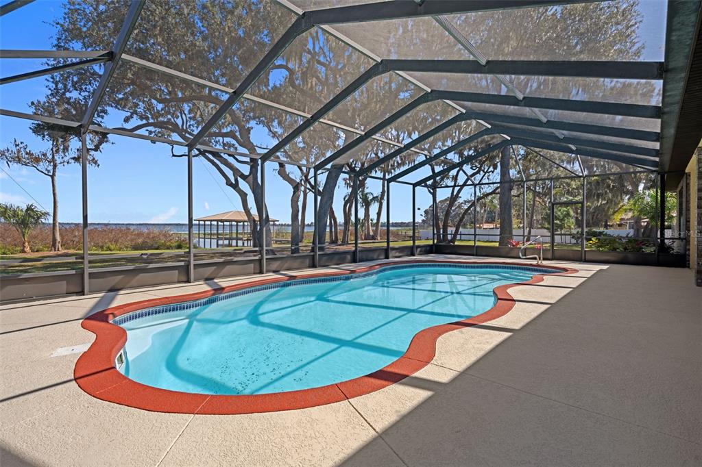 A screened-in swimming pool with a red border sits on a patio overlooking a lake — 4300 TIMBERLANE ROAD, LAKE WALES, FL