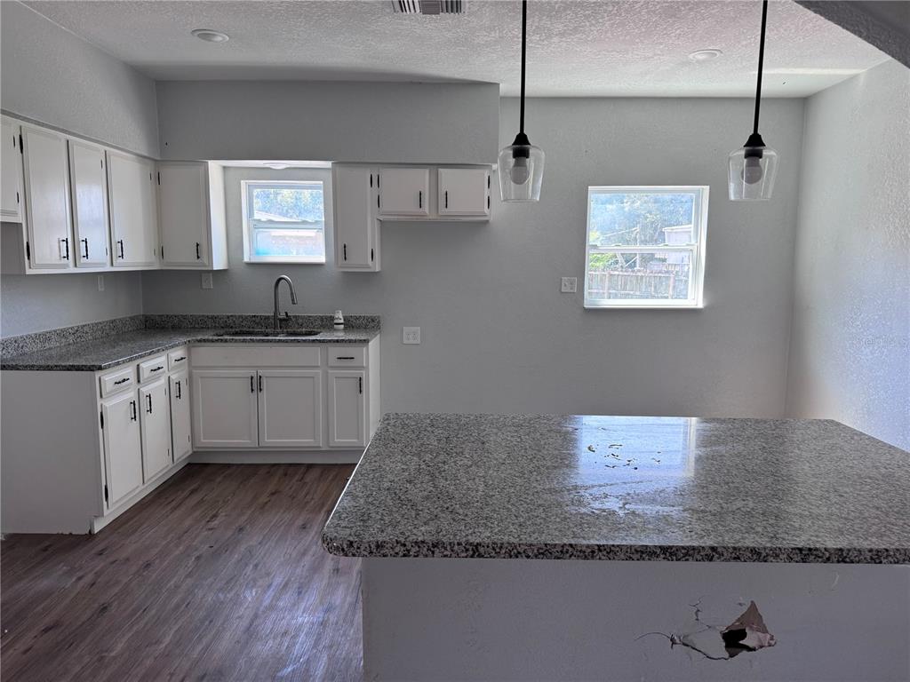 A kitchen features white cabinets, granite countertops, wood-look flooring, and a central island — 1142 SW MILDRED STREET, ARCADIA, FL