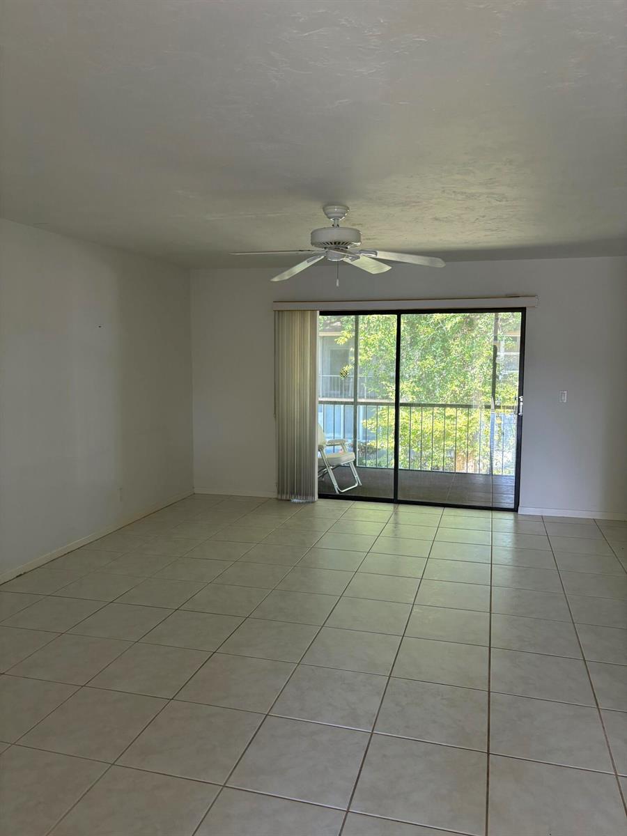 An empty living room features white walls, light-colored tile flooring, a ceiling fan, and sliding doors — 1700 Dover Road # a, Delray Beach FL 33445, DELRAY BEACH, FL