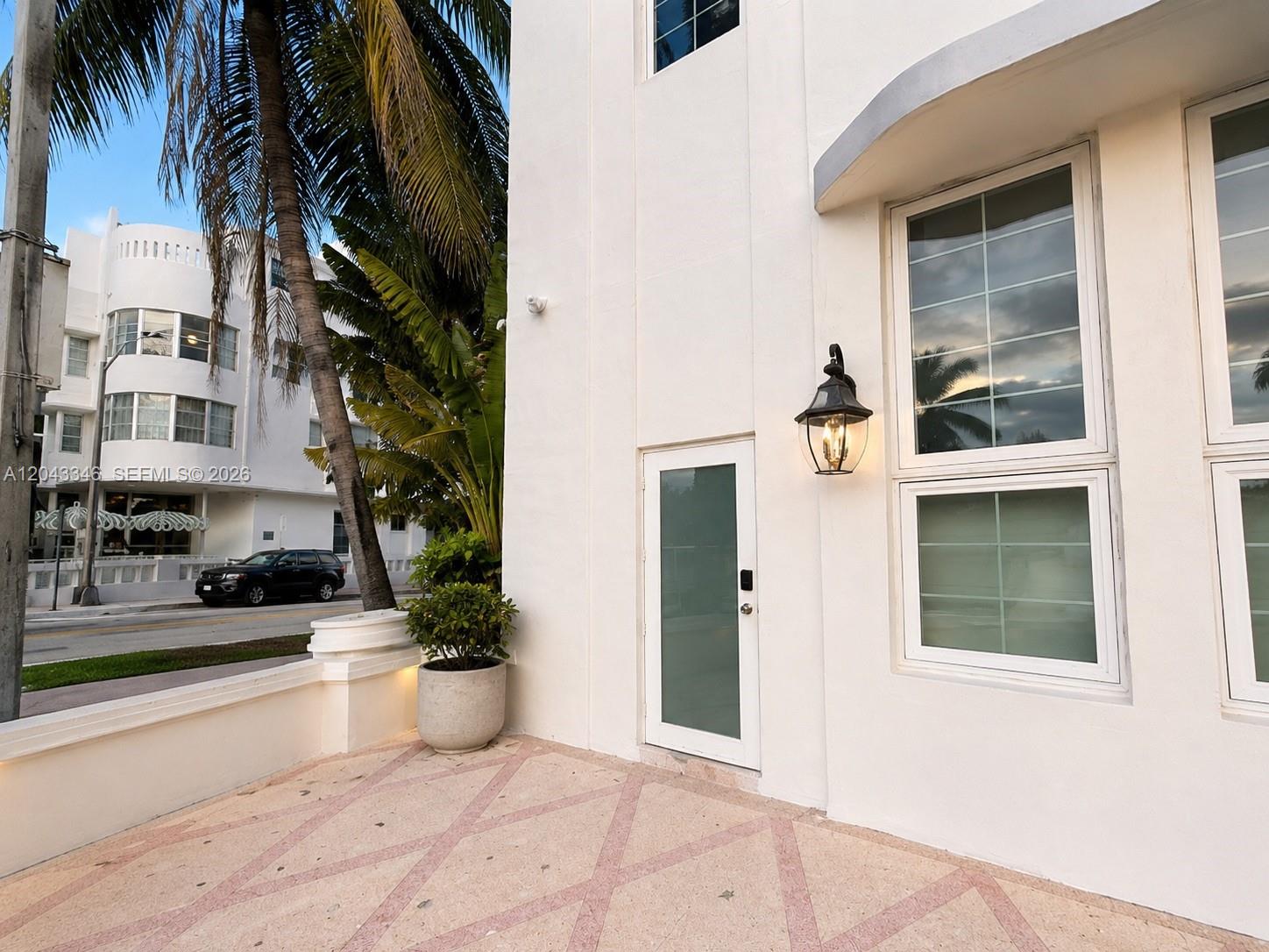 A white building exterior features a frosted glass door, a wall lantern, and a patio — 3025 Indian Creek Dr # 110, Miami Beach FL 33140, MIAMI BEACH, FL