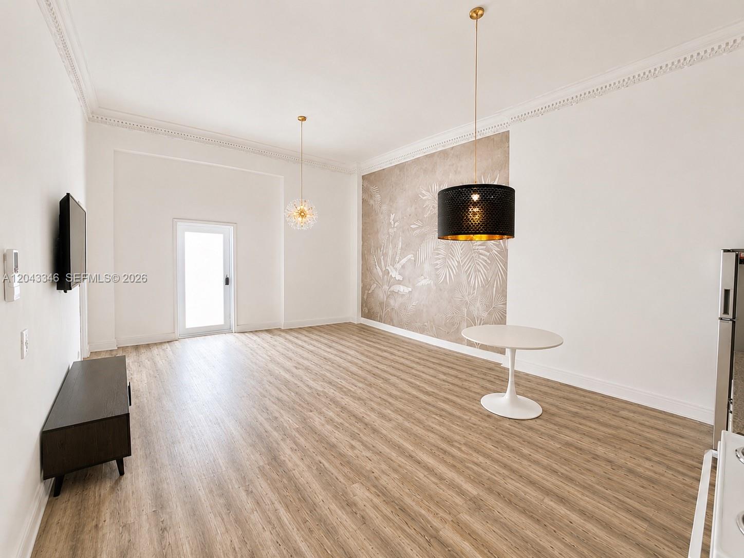 An open living area features wood-look flooring, a patterned accent wall, and two pendant lights — 3025 Indian Creek Dr # 110, Miami Beach FL 33140, MIAMI BEACH, FL