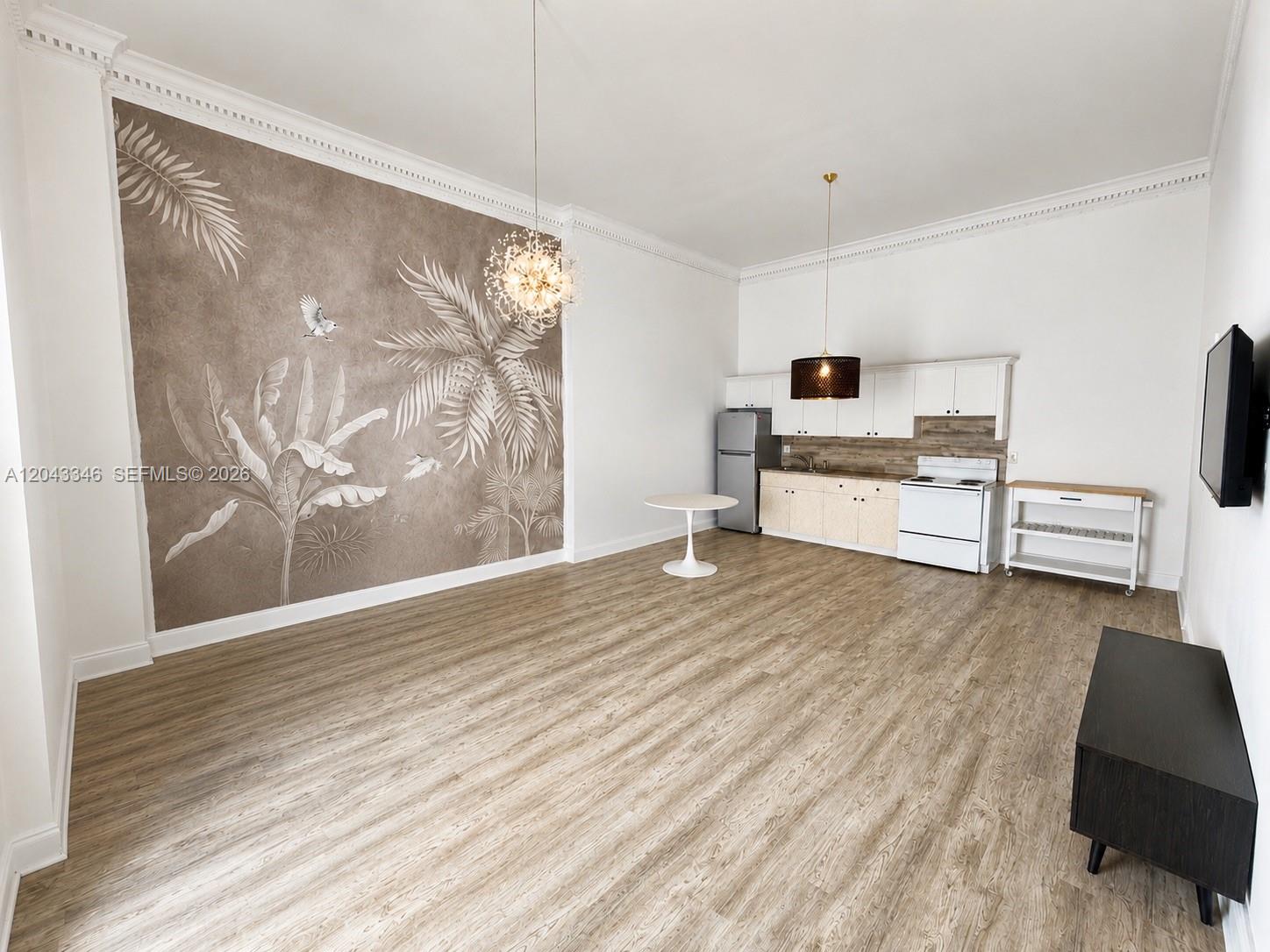 This open-plan living area features a kitchen, wood-look flooring, and a large tropical-themed mural — 3025 Indian Creek Dr # 110, Miami Beach FL 33140, MIAMI BEACH, FL