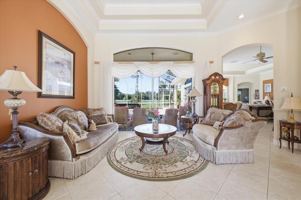 A living room features a tray ceiling, tile floors, and a large window overlooking a pool — 2309 LITTLE COUNTRY ROAD, PARRISH, FL