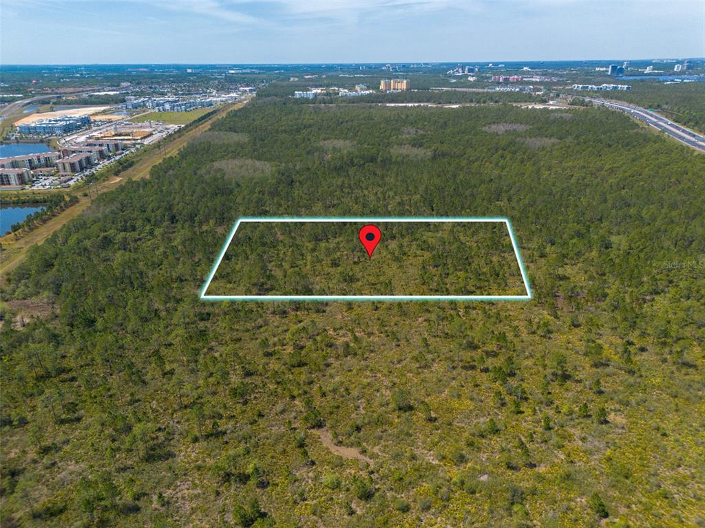 An aerial view shows a rectangular plot of land outlined in blue within a forest — SR-535, ORLANDO, FL
