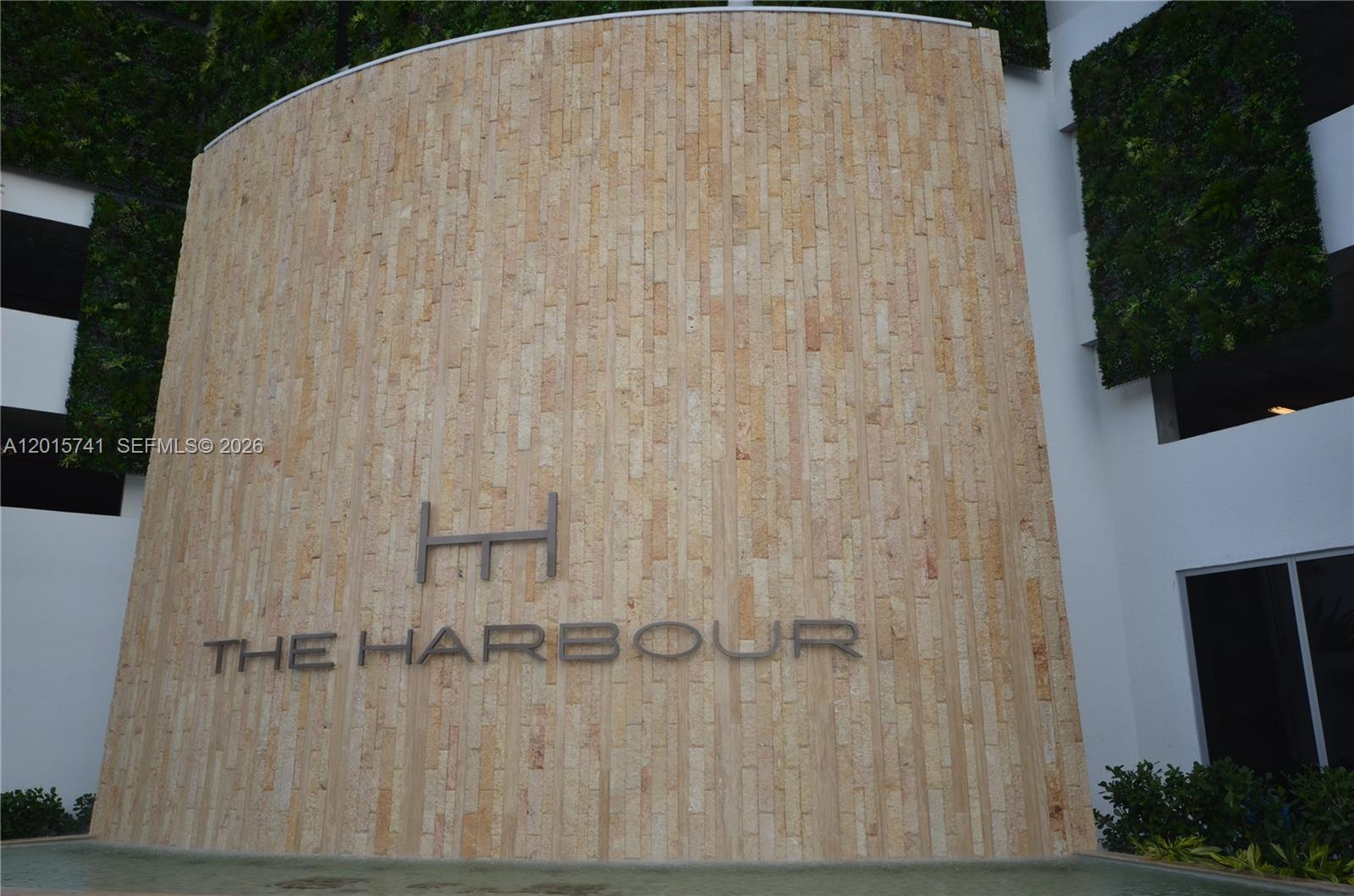 A curved stone wall features the metal logo and name for The Harbour building — 16385 Biscayne Blvd # 519, North Miami Beach FL 33160, NORTH MIAMI BEACH, FL
