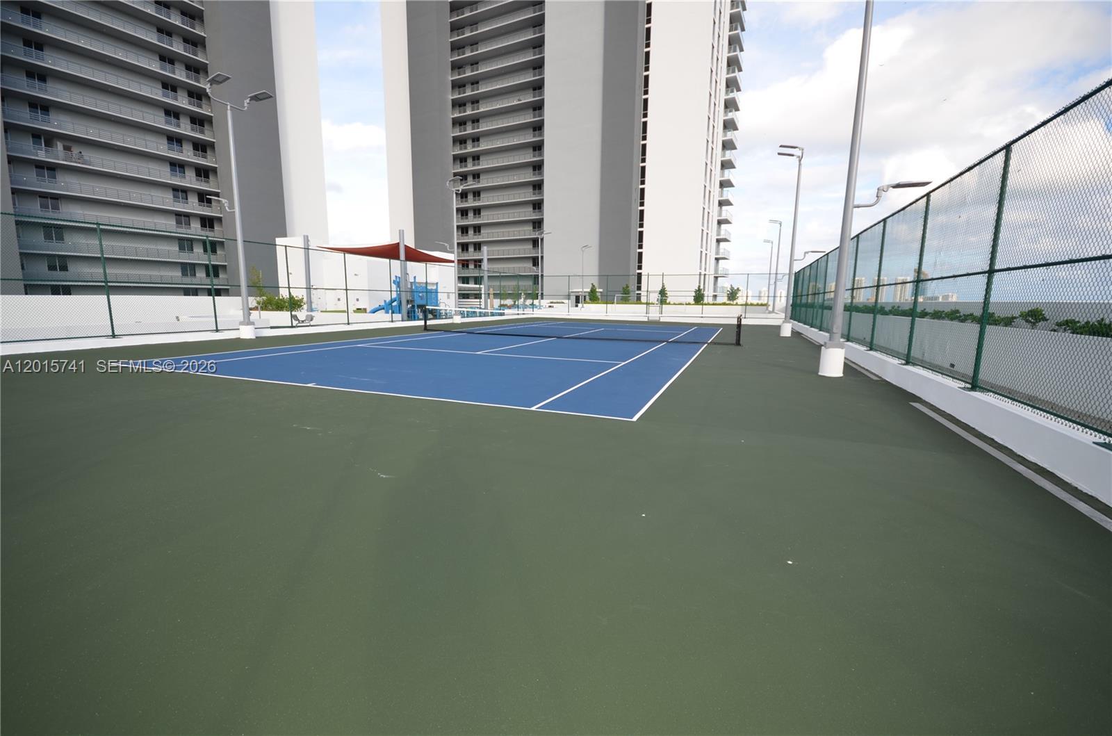 An outdoor tennis court with a blue surface surrounded by high chain-link fencing — 16385 Biscayne Blvd # 519, North Miami Beach FL 33160, NORTH MIAMI BEACH, FL