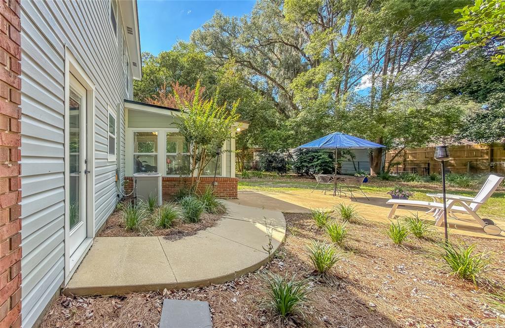 A backyard patio with a blue umbrella, lounge chair, and landscaping next to a house — 2210 WALL STREET, TALLAHASSEE, FL