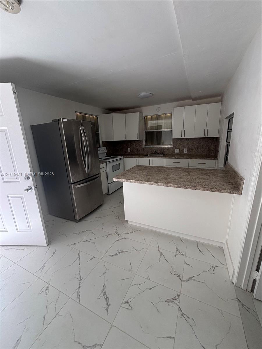 A kitchen features white cabinets, stainless steel appliances, a breakfast bar, and marble-patterned tile flooring — 116 Allen Rd, West Park FL 33023, WEST PARK, FL