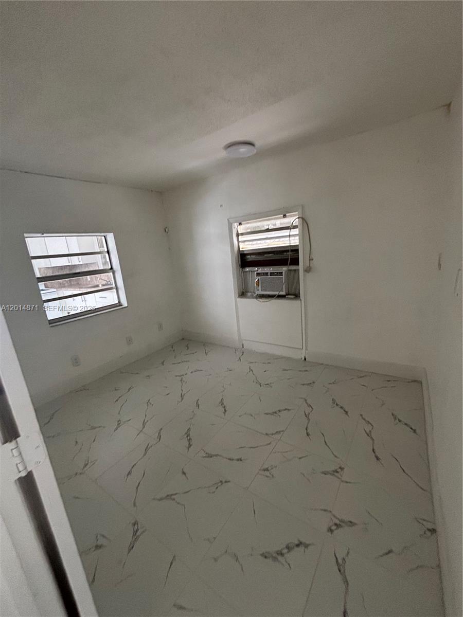 An empty room features white marble-patterned tile flooring, two windows, and a wall-mounted air conditioner — 116 Allen Rd, West Park FL 33023, WEST PARK, FL