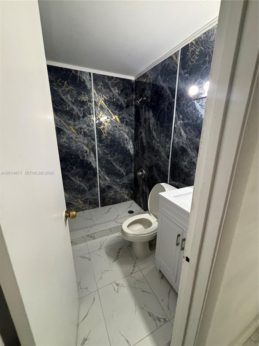 A small bathroom features a white vanity, a toilet, and dark marble-patterned shower walls — 116 Allen Rd, West Park FL 33023, WEST PARK, FL