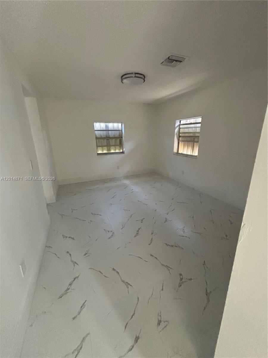 An empty room features white walls, a ceiling light fixture, and white marble-patterned tile flooring — 116 Allen Rd, West Park FL 33023, WEST PARK, FL