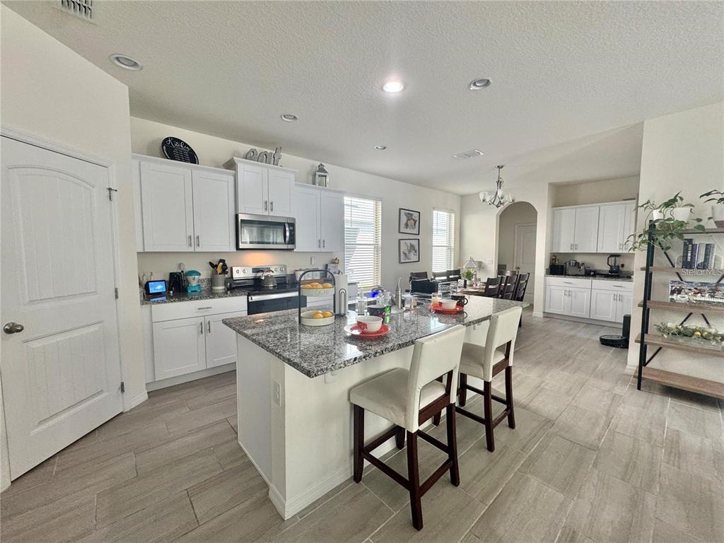 A kitchen with white cabinets, granite countertops, a central island, and tile flooring — 16031 SCARPETTA STREET, WINTER GARDEN, FL