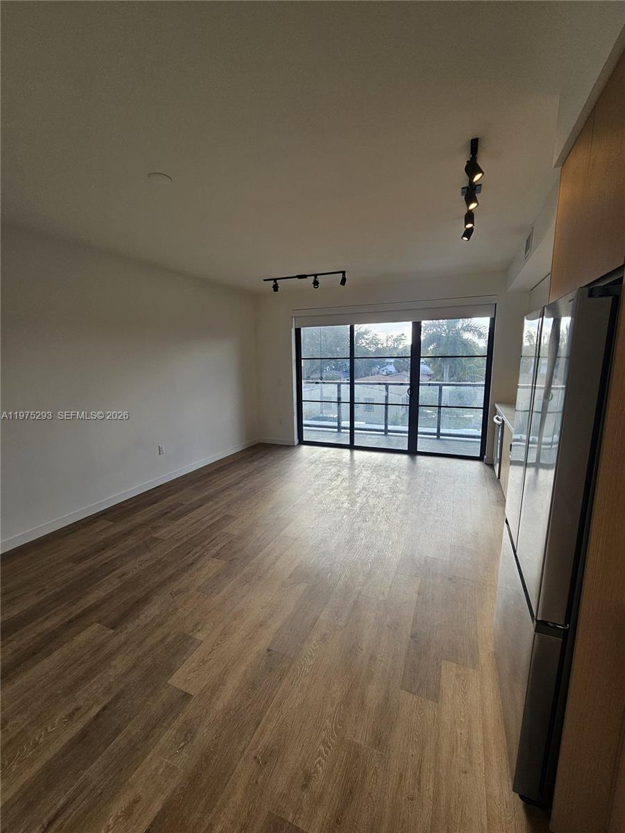 An open living area features wood-look flooring, track lighting, and a sliding glass door balcony — 1650 NE 124th St # 246, North Miami FL 33181, NORTH MIAMI, FL
