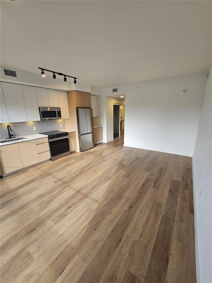 A modern kitchen with light wood cabinets and stainless steel appliances opens into a living area — 1650 NE 124th St # 246, North Miami FL 33181, NORTH MIAMI, FL