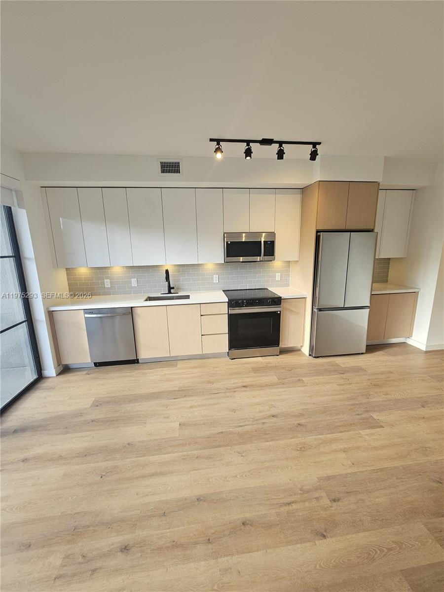 A modern kitchen features light wood lower cabinets, white upper cabinets, and stainless steel appliances — 1650 NE 124th St # 246, North Miami FL 33181, NORTH MIAMI, FL