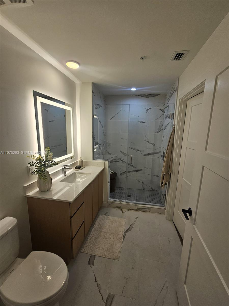 A modern bathroom features a wood vanity, a backlit mirror, and a glass-enclosed walk-in shower — 1650 NE 124th St # 246, North Miami FL 33181, NORTH MIAMI, FL