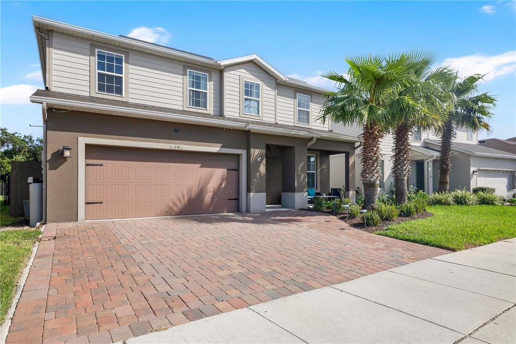 A two-story house with a brown garage, beige siding, and a brick paver driveway — 17096 GOLDCREST LOOP, CLERMONT, FL