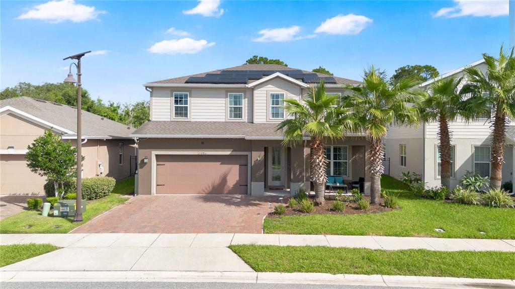 A two-story suburban house features a brick driveway, a two-car garage, and solar panels — 17096 GOLDCREST LOOP, CLERMONT, FL