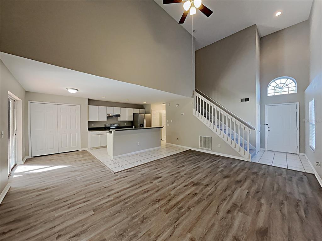 An open-concept living area features wood-look flooring, a kitchen with white cabinets, and a staircase — 2184 HEATHWOOD CIRCLE, ORLANDO, FL