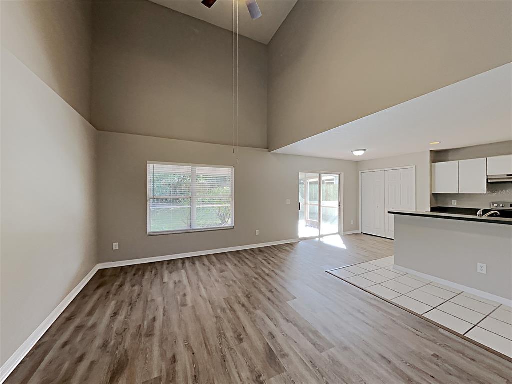 A living room with high ceilings, wood-look flooring, and an adjacent kitchen with tile flooring — 2184 HEATHWOOD CIRCLE, ORLANDO, FL
