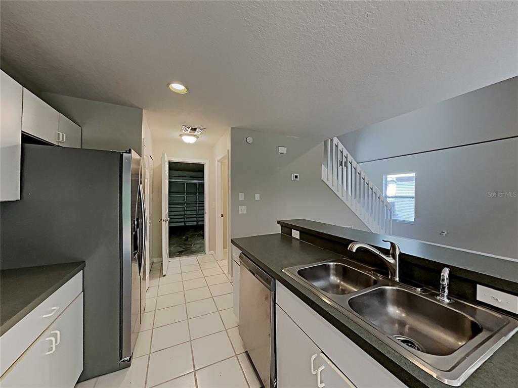 A kitchen with white cabinets, stainless steel appliances, and tile flooring leads to a staircase — 2184 HEATHWOOD CIRCLE, ORLANDO, FL