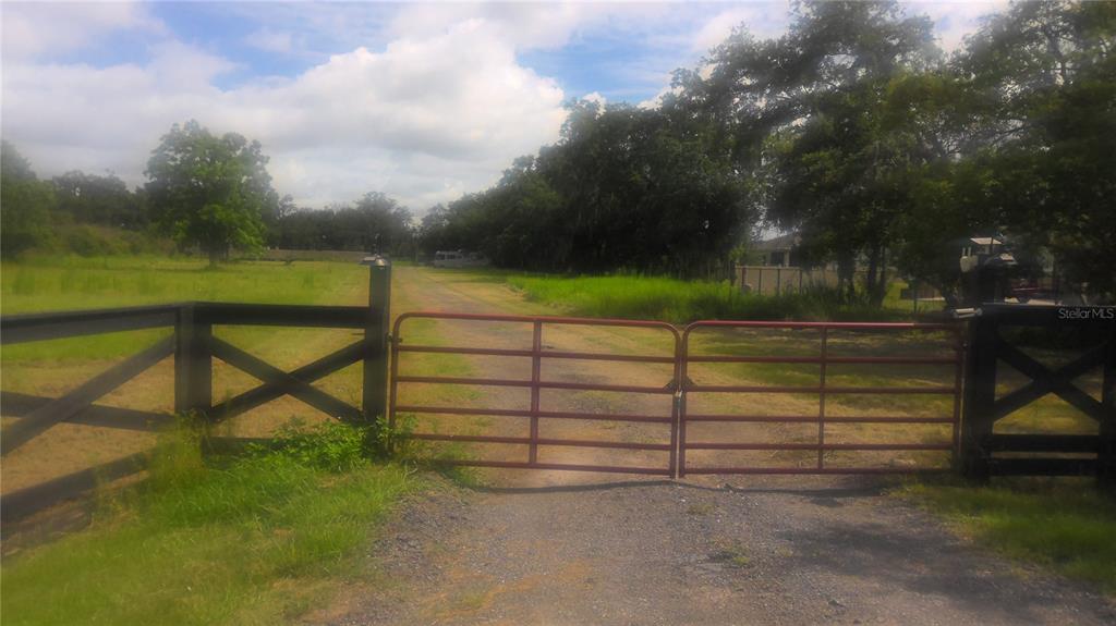 A red metal gate stands at the entrance of a gravel driveway on a grassy lot — 2875 SHARP ROAD, KISSIMMEE, FL