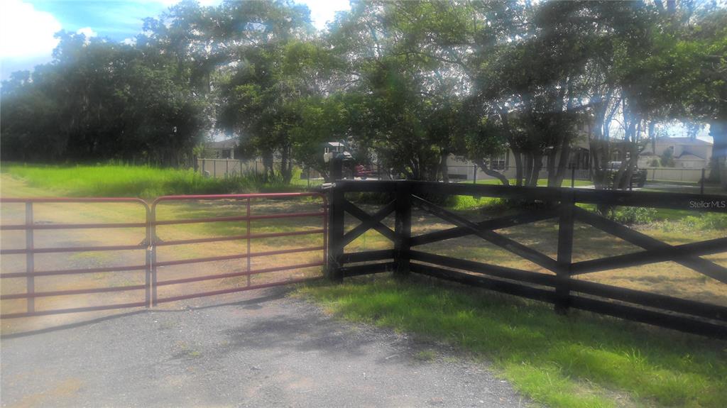 A red metal gate opens to a gravel driveway beside a black wooden fence — 2875 SHARP ROAD, KISSIMMEE, FL