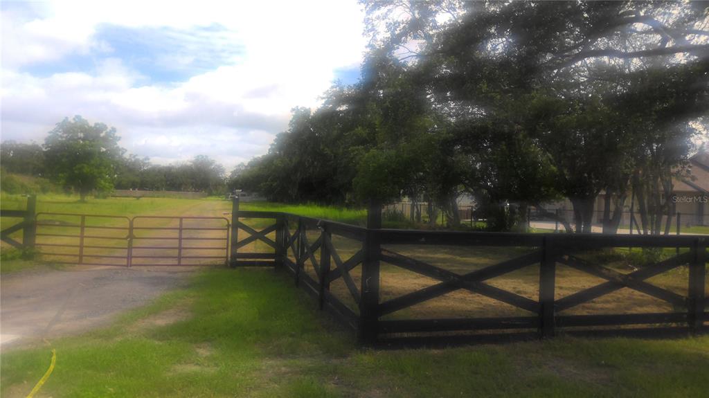 A black wooden cross-buck fence borders a gravel driveway leading to a metal gate — 2875 SHARP ROAD, KISSIMMEE, FL