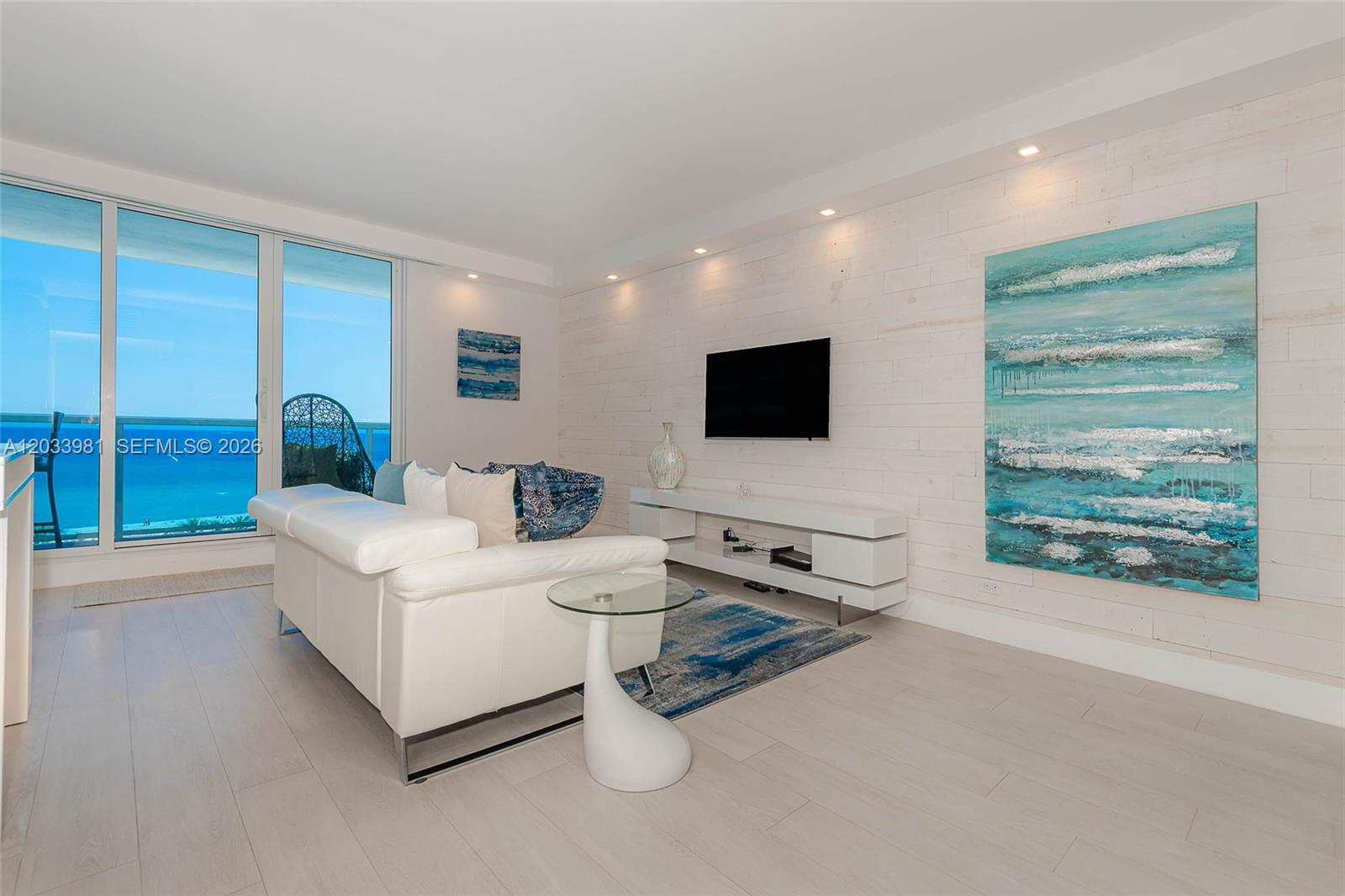 A modern living room features a white sofa, a wall-mounted television, and ocean views — 2301 Collins Ave # 941, Miami Beach FL 33139, MIAMI BEACH, FL