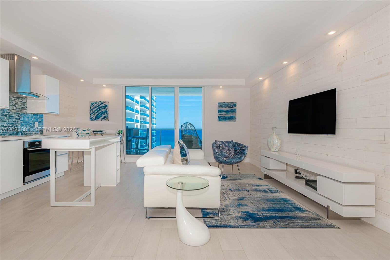 A modern living room and kitchen area features white furniture, blue accents, and ocean views — 2301 Collins Ave # 941, Miami Beach FL 33139, MIAMI BEACH, FL