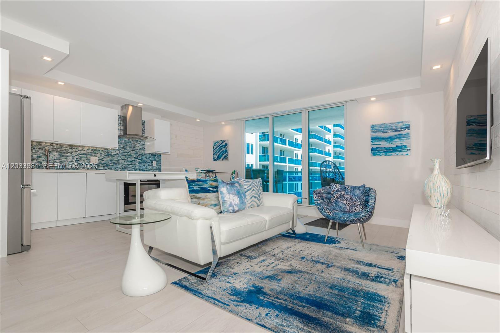 A modern living room features a white sofa, blue patterned rug, and an open kitchen — 2301 Collins Ave # 941, Miami Beach FL 33139, MIAMI BEACH, FL