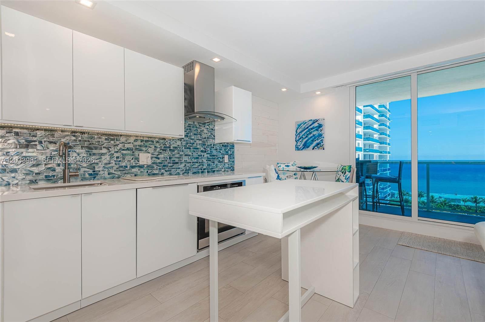 A modern kitchen features white cabinetry, a blue mosaic backsplash, and a balcony with ocean views — 2301 Collins Ave # 941, Miami Beach FL 33139, MIAMI BEACH, FL