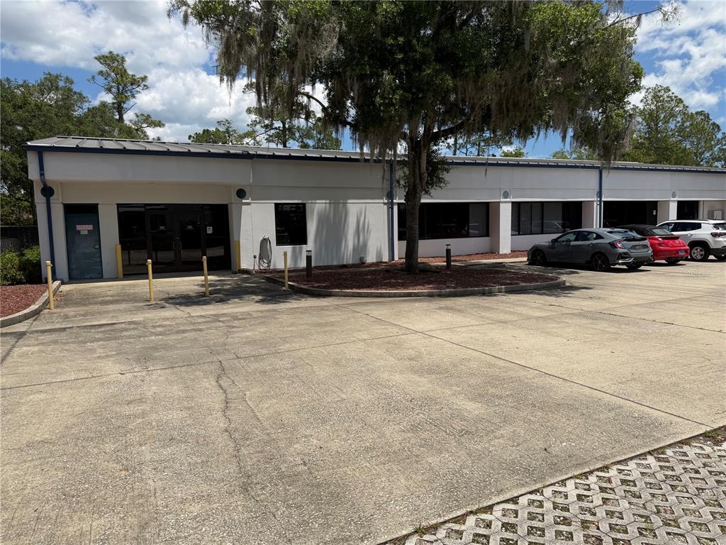 A single-story commercial building with a concrete parking lot and a large shade tree — 2 MCCORMICK DRIVE, PALM COAST, FL