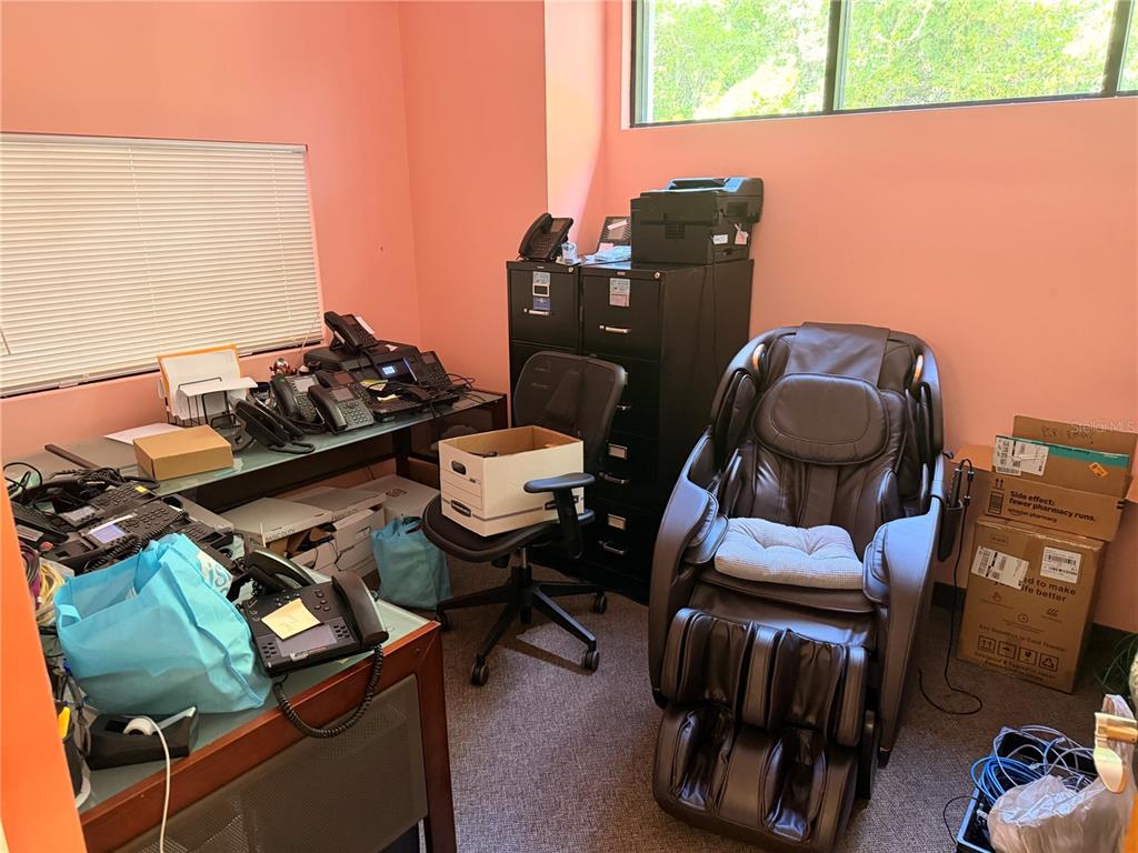 An office room contains multiple desk phones, a black filing cabinet, and a massage chair — 2 MCCORMICK DRIVE, PALM COAST, FL