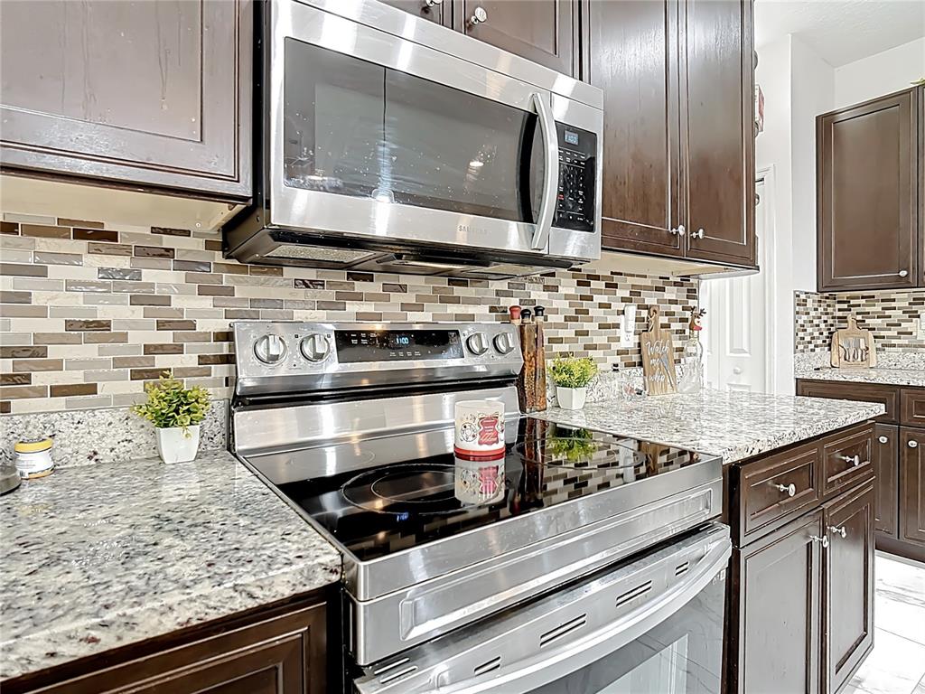 A kitchen features dark wood cabinets, granite countertops, a stainless steel stove, and mosaic backsplash — 471 GANNET COURT, POINCIANA, FL