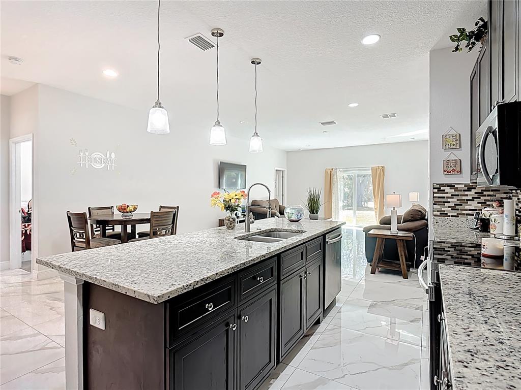 A kitchen island with granite countertops and dark cabinets sits in an open-concept living area — 471 GANNET COURT, POINCIANA, FL