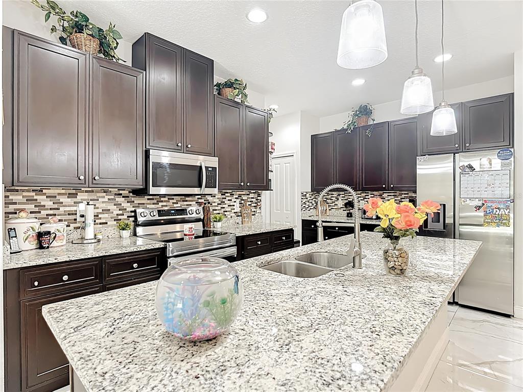 A kitchen features dark wood cabinets, granite countertops, a large island, and stainless steel appliances — 471 GANNET COURT, POINCIANA, FL