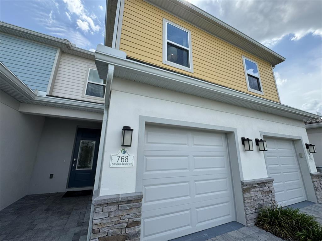 A two-story townhouse exterior features yellow siding, a white stucco garage, and stone accents — 768 DRIVING RANGE COURT, KISSIMMEE, FL