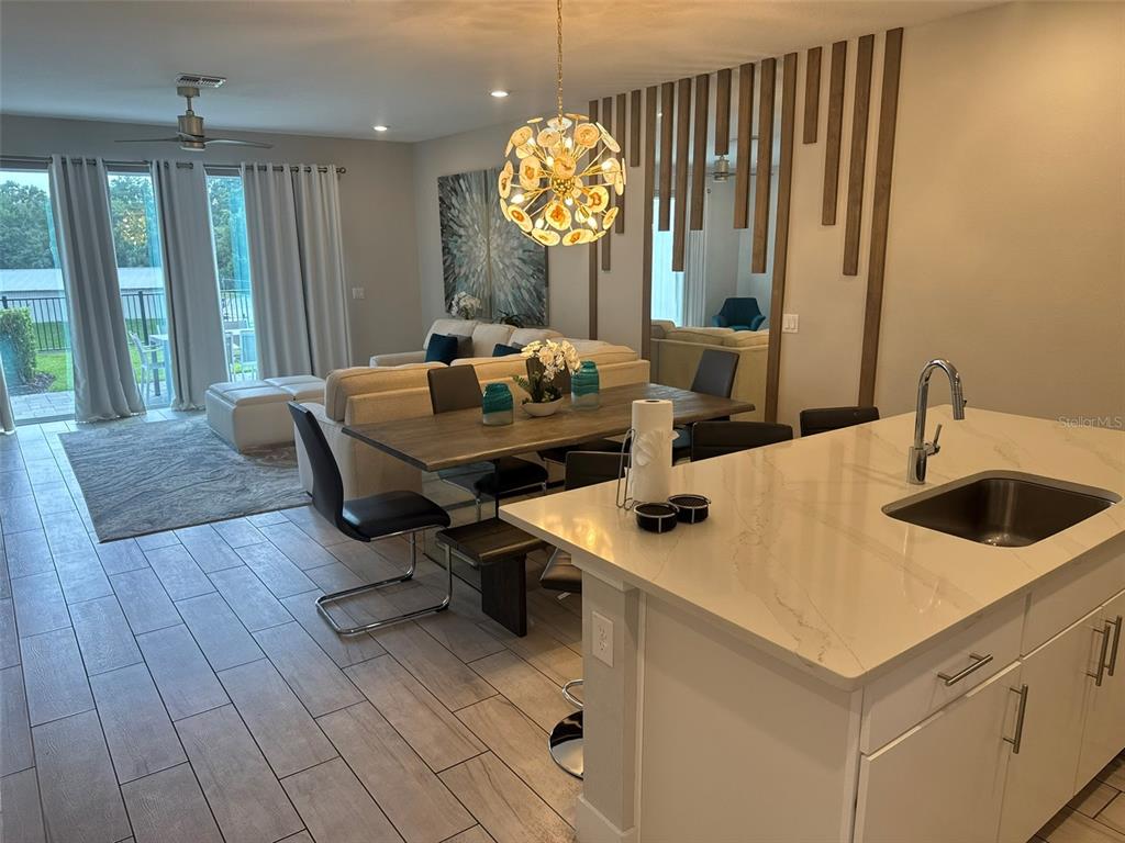 An open-concept kitchen and dining area features a quartz island, wood-slat wall, and modern chandelier — 768 DRIVING RANGE COURT, KISSIMMEE, FL