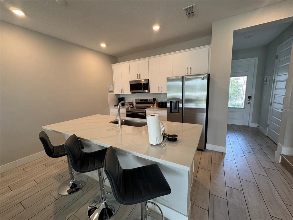 A modern kitchen features white cabinetry, stainless steel appliances, and a large quartz-topped island — 768 DRIVING RANGE COURT, KISSIMMEE, FL